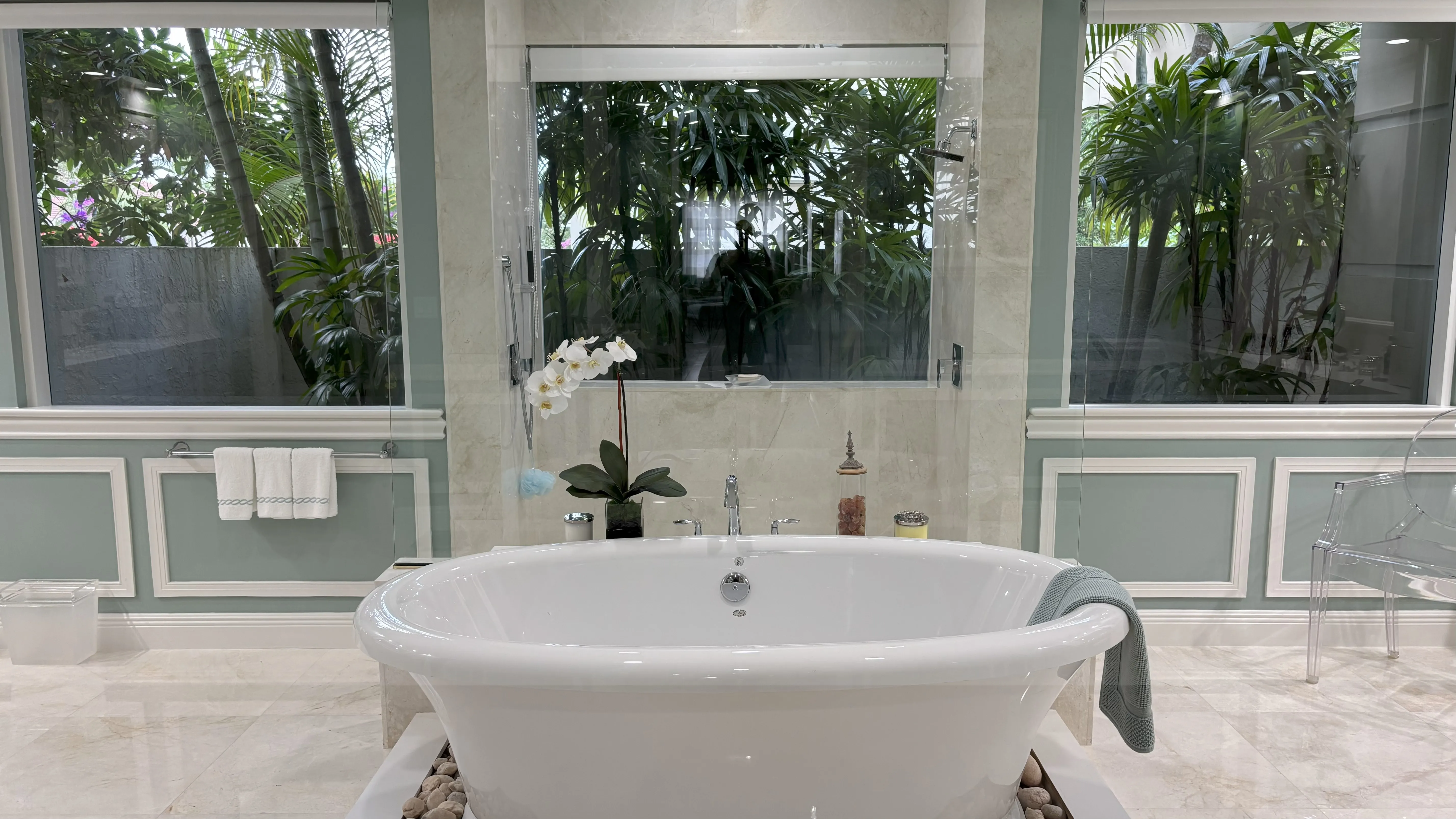 Elegant freestanding bathtub surrounded by large windows and lush greenery